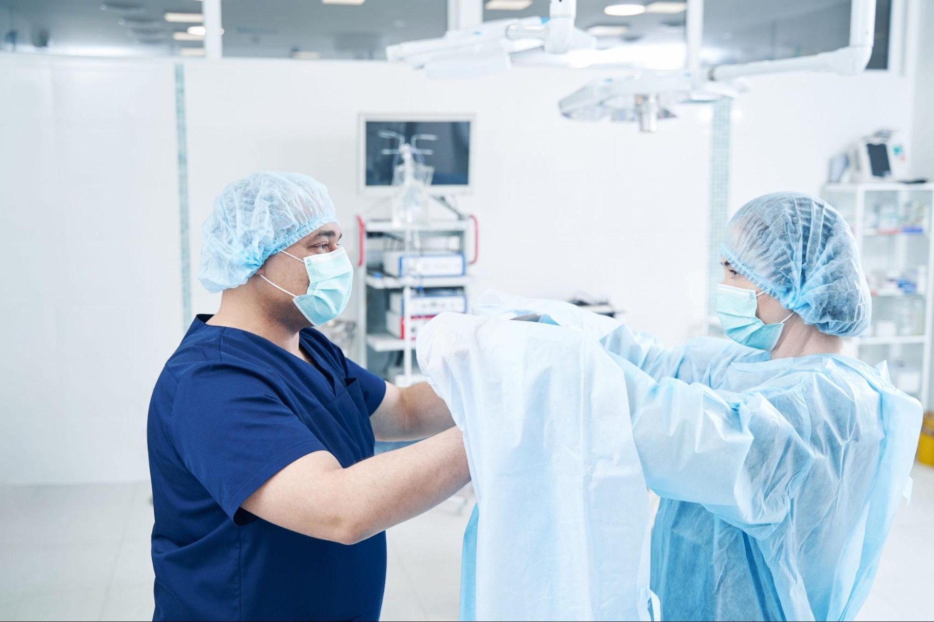 Operating room nurse helping a surgeon into a sterile gown before a procedure